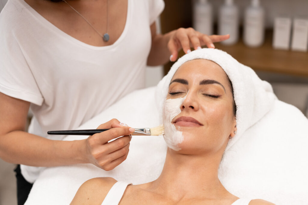 Aesthetics applying a mask to the face of a Middle-aged woman in modern wellness center. Beauty and Aesthetic concepts.